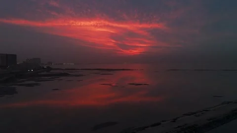 Dramatic red sunset over calm sea with reflections and coastal skyline Stock Footage 329584382