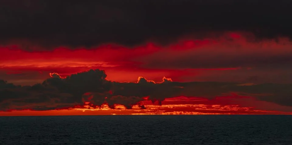 Dramatic red sunset over the ocean with dark clouds creating a fiery sky 库存照片