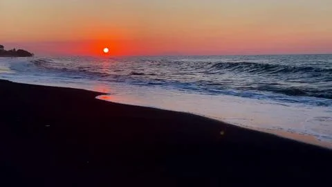 Dramatic Red Sunset Over Ocean Waves on Black Sand Beach in Bali Stock Photos