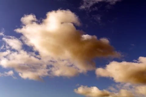 Dramatic Reddish Brown and white fluffy clouds in blue sky Stock Photos