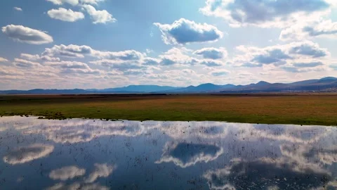 Dramatic reflection of white clouds on a calm wetland surface with distant mount Stock Footage 332726225