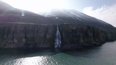 Dramatic revolving aerial shot of waterfall flowing into ocean over cliffs. Video stock 166309455
