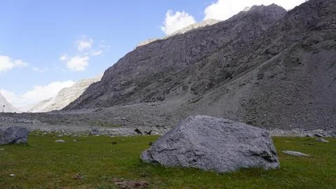 Dramatic rocky cliff face, large gray boulder on bright green grass. Stock Photos