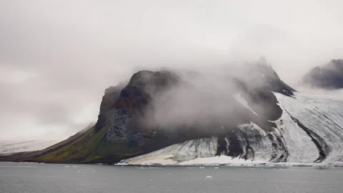 A dramatic, rocky coastal landscape partially shrouded in mist and clouds, with Stock Footage 312209463