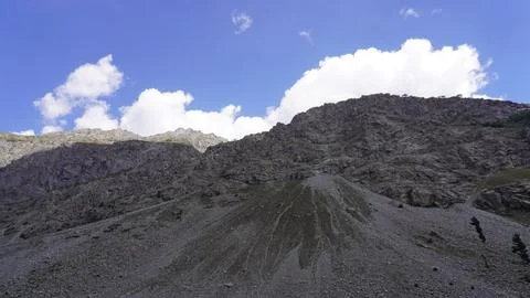 Dramatic rocky mountain slopes and scree against blue sky, white clouds. Stock Photos
