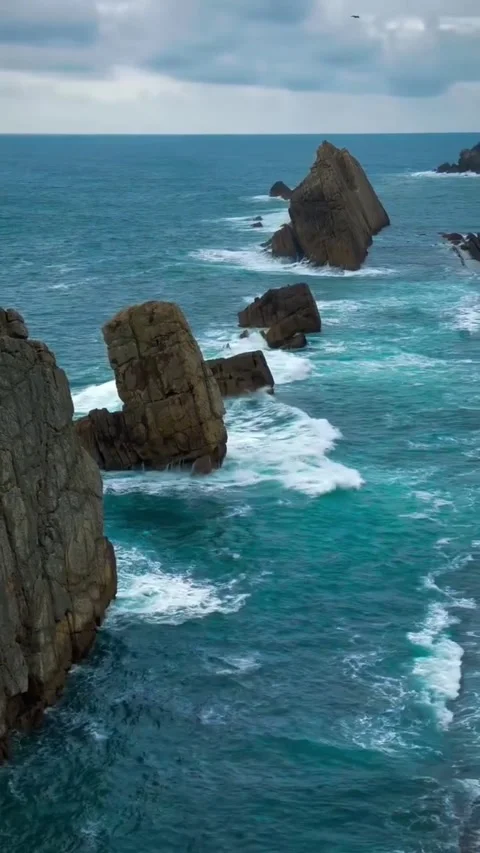 Dramatic rocky sea stacks rising from the turquoise ocean waves along a rugged Vidéo 334163759