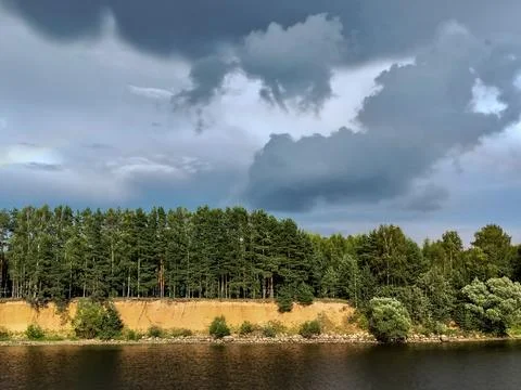 Dramatic scene dark storm clouds over a pine forest on a riverbank Stock Photos