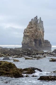 Dramatic sea stack rock formation on rocky coastline under cloudy sky Stock Photos