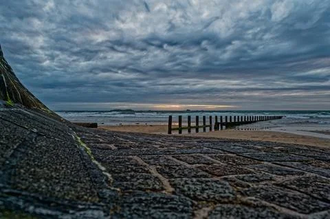 Dramatic seascape with feather clouds. Rocky coastline with wooden breakwaters Foto stock