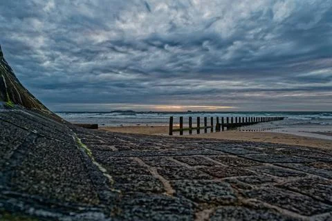 Dramatic seascape with feather clouds. Rocky coastline with wooden breakwa... Stock Photos