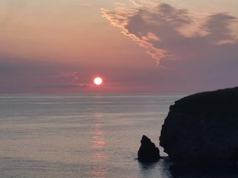 Dramatic Seascape Sunset with Cliff Silhouette - The vibrant red sun dips b.. Stock Photos