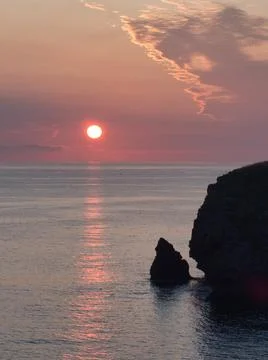 Dramatic Seascape Sunset with Cliff Silhouette - The vibrant red sun dips b.. Stock Photos