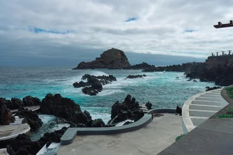 Dramatic seascape with volcanic rocks and vibrant turquoise waves under a c.. Stock Photos