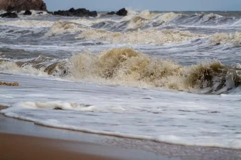 Dramatic seaside scene with waves crashing on sandy beach beneath moody clo.. Stock Photos