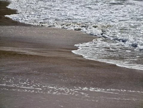 Dramatic shoreline image showcasing frothy surf meeting shadowed sands with Stock Photos