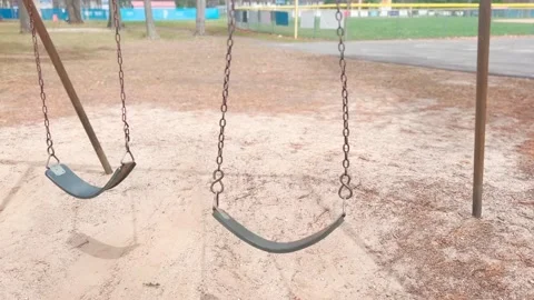 DRAMATIC SHOT OF EMPTY PLAYGROUND SWING SET IN MOTION Stock Footage 182480613