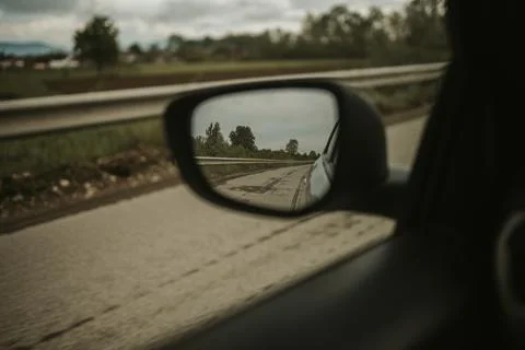 A dramatic shot of the side mirror of a car reflecting the countryside road a Stock Photos