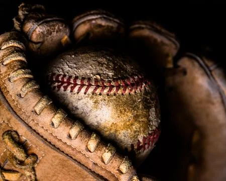 Dramatic side lighting on old baseball caught in worn out mitt. Stock Photos