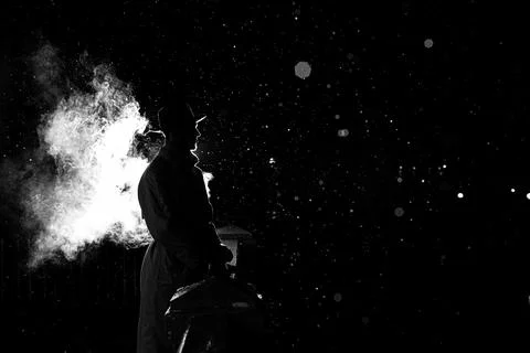 Dramatic silhouette of a dangerous man in a hat at night in the rain in the city Stock Photos