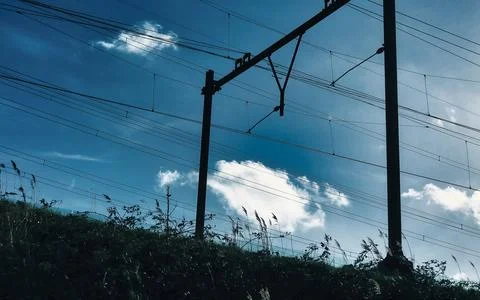 Dramatic Silhouette of Overhead Train Power Lines Against a Blue Sky with C.. Stock Photos