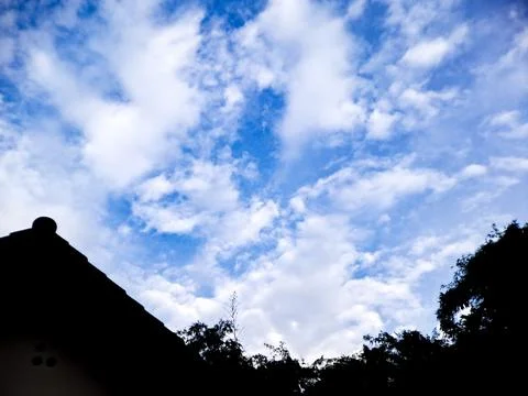Dramatic silhouette of rooftops and a tree against a vibrant blue sky with .. Stock Photos