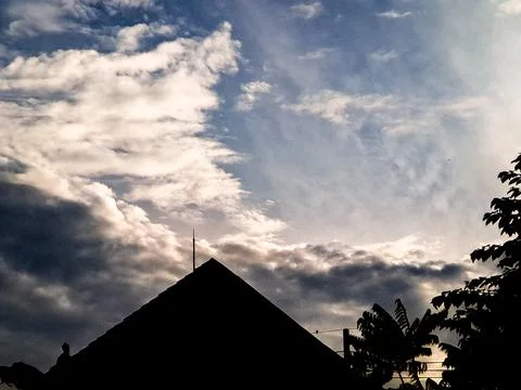 Dramatic silhouette of rooftops and a tree against a vibrant blue sky with .. Stock Photos