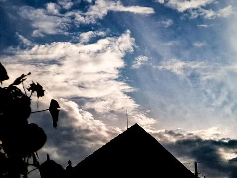 Dramatic silhouette of rooftops and a tree against a vibrant blue sky with .. Stock Photos