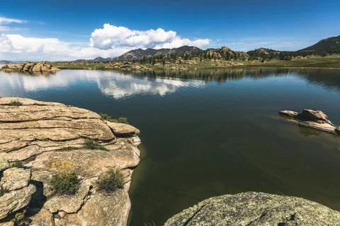 Dramatic sky and clouds reflecting over a large mountain lake with calm waters Stock Photos