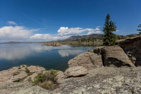 Dramatic sky and clouds reflecting over a large mountain lake with calm waters Stock Photos
