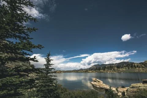 Dramatic sky and clouds reflecting large mountain lake calm forest of trees Stock Photos