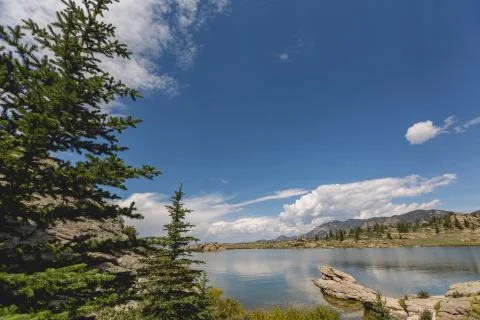 Dramatic sky and clouds reflecting over large mountain lake forest of pine trees Stock Photos