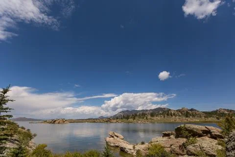 Dramatic sky and clouds reflecting over large mountain lake forest of pine trees Stock Photos