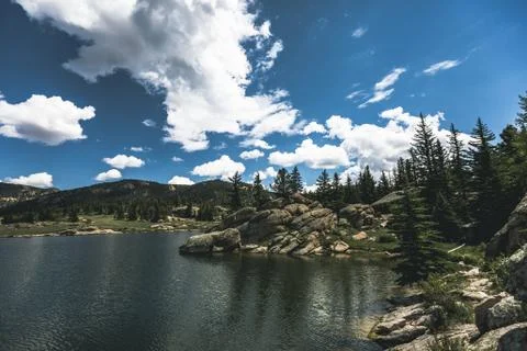 Dramatic sky and clouds reflecting over large mountain lake forest of pine trees Stock Photos