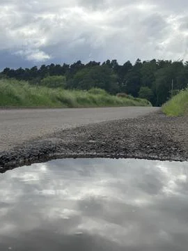 Dramatic Sky and Clouds Reflection in a Rain Water Puddle on Countryside Road. 写真素材