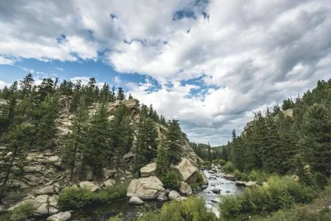 Dramatic sky and raging river running through a forest and valley with mountains Stock Photos