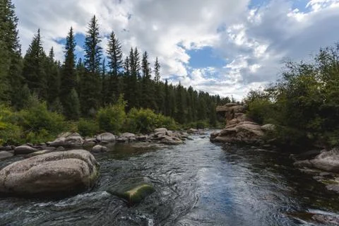 Dramatic sky and raging river running through a forest and valley with mountains Stock Photos
