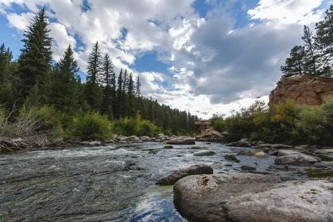 Dramatic sky and raging river running through a forest and valley with mountains Stock Photos
