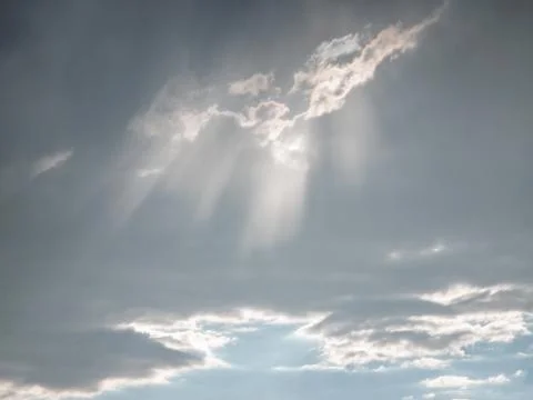 Dramatic sky with beams of sunlight piercing through scattered gray clouds 写真素材