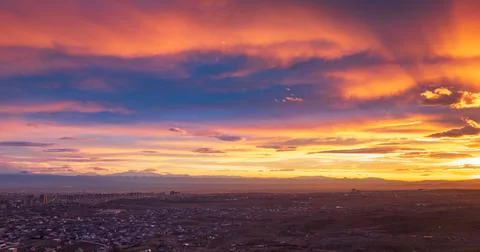 Dramatic sky with clouds painted in sunset hues over cityscape Stock Photos