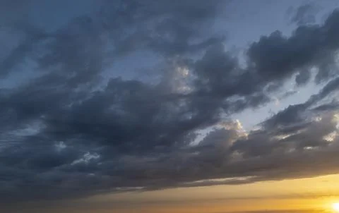 Dramatic sky with dark clouds illuminated by a warm sunset glow creates a Stock Photos