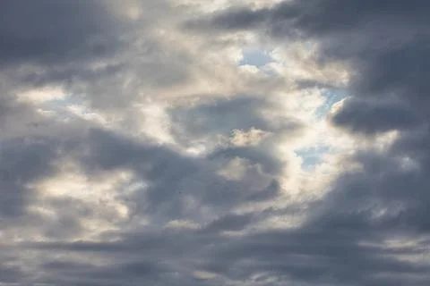 Dramatic sky with dark clouds parting to reveal bright sunlight and blue sky Stock Photos