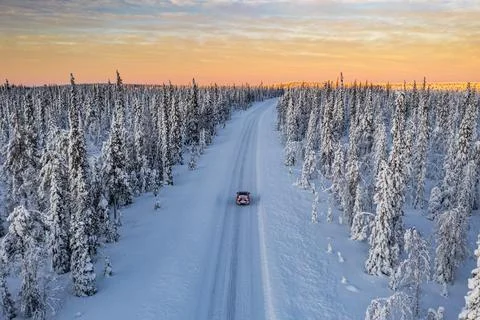 Dramatic sky at dawn over a car traveling into the snowy forest, aerial view, Stock Photos
