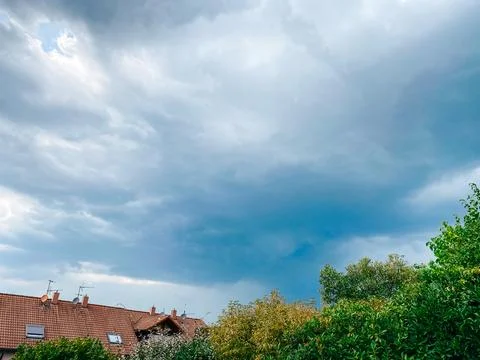 Dramatic sky filled with dark clouds looms over rooftops and lush greenery, Stock Photos