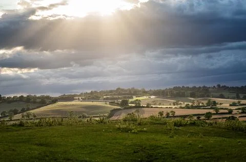 Dramatic sky with golden sunlight rays breaking through dark storm clouds over Stock Photos