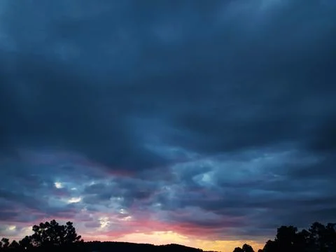 Dramatic sky with moody, dark clouds illuminated by soft sunset hues. Evoke.. Stock Photos