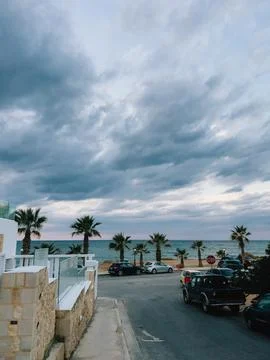 Dramatic sky over beach with palm trees. Parked cars lining beach, surrounded by Stock Photos