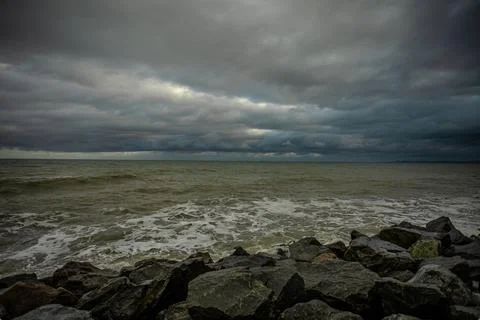 Dramatic sky over the black sea with waves, clouds and stones Stock Photos