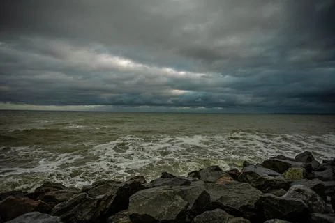 Dramatic sky over the black sea with waves, clouds and stones Stock Photos