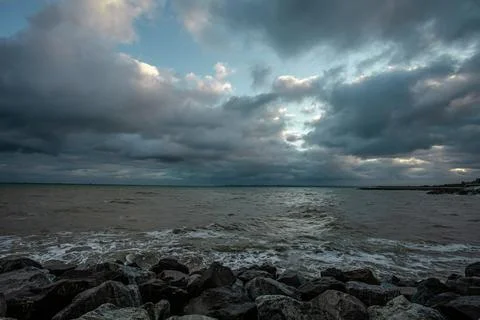 Dramatic sky over the black sea with waves, clouds and stones Stock Photos