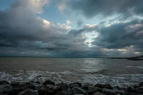 Dramatic sky over the black sea with waves, clouds and stones Stock Photos